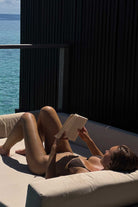 Person reading a book on a sunlit outdoor sofa with ocean view