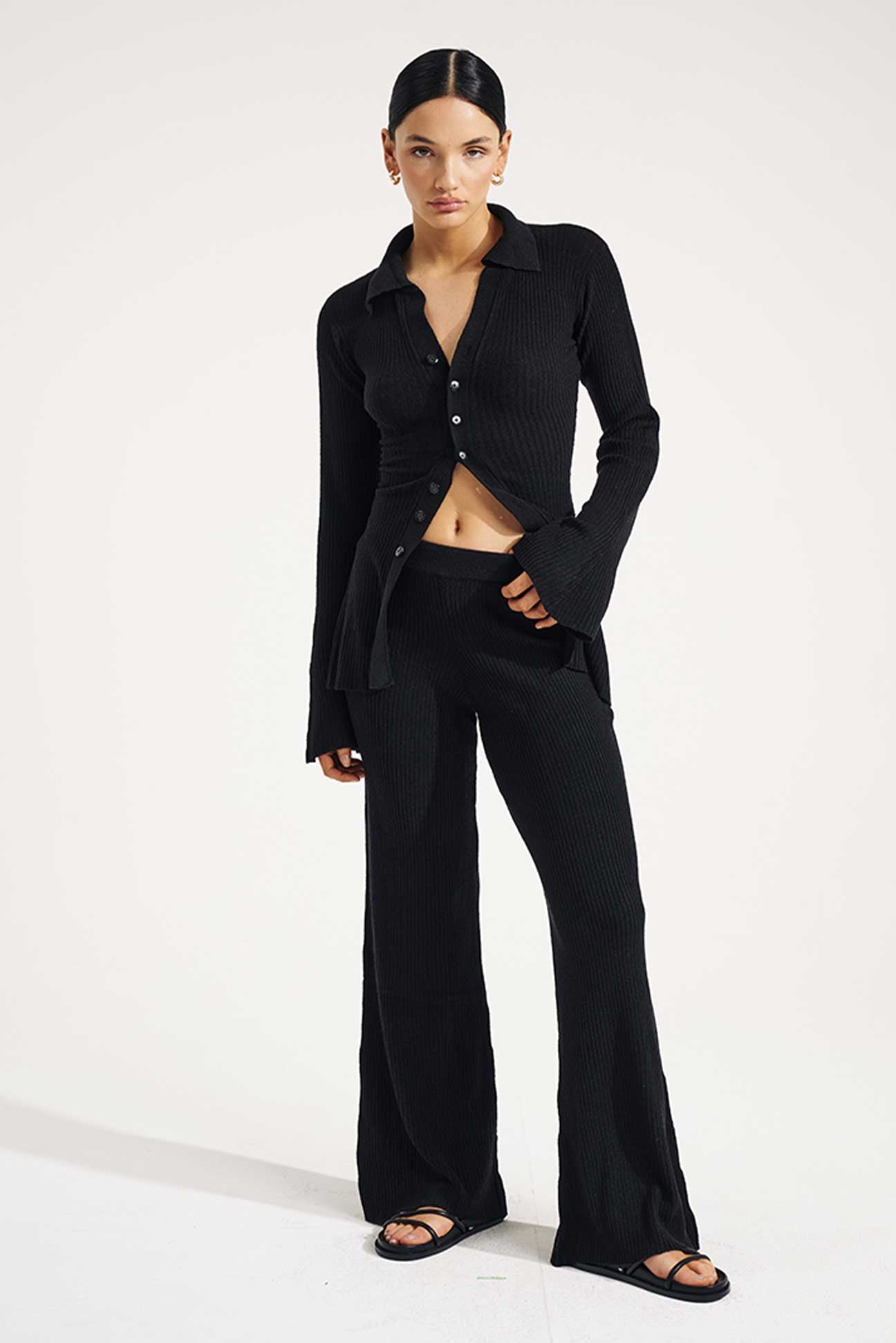 Woman wearing a black outfit with a buttoned shirt and wide-leg pants on a white background