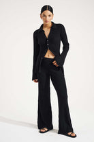 Woman wearing a black outfit with a buttoned shirt and wide-leg pants on a white background
