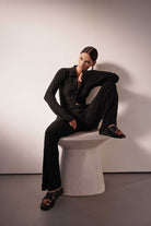 Person wearing a black outfit sitting on a white stool against a plain background