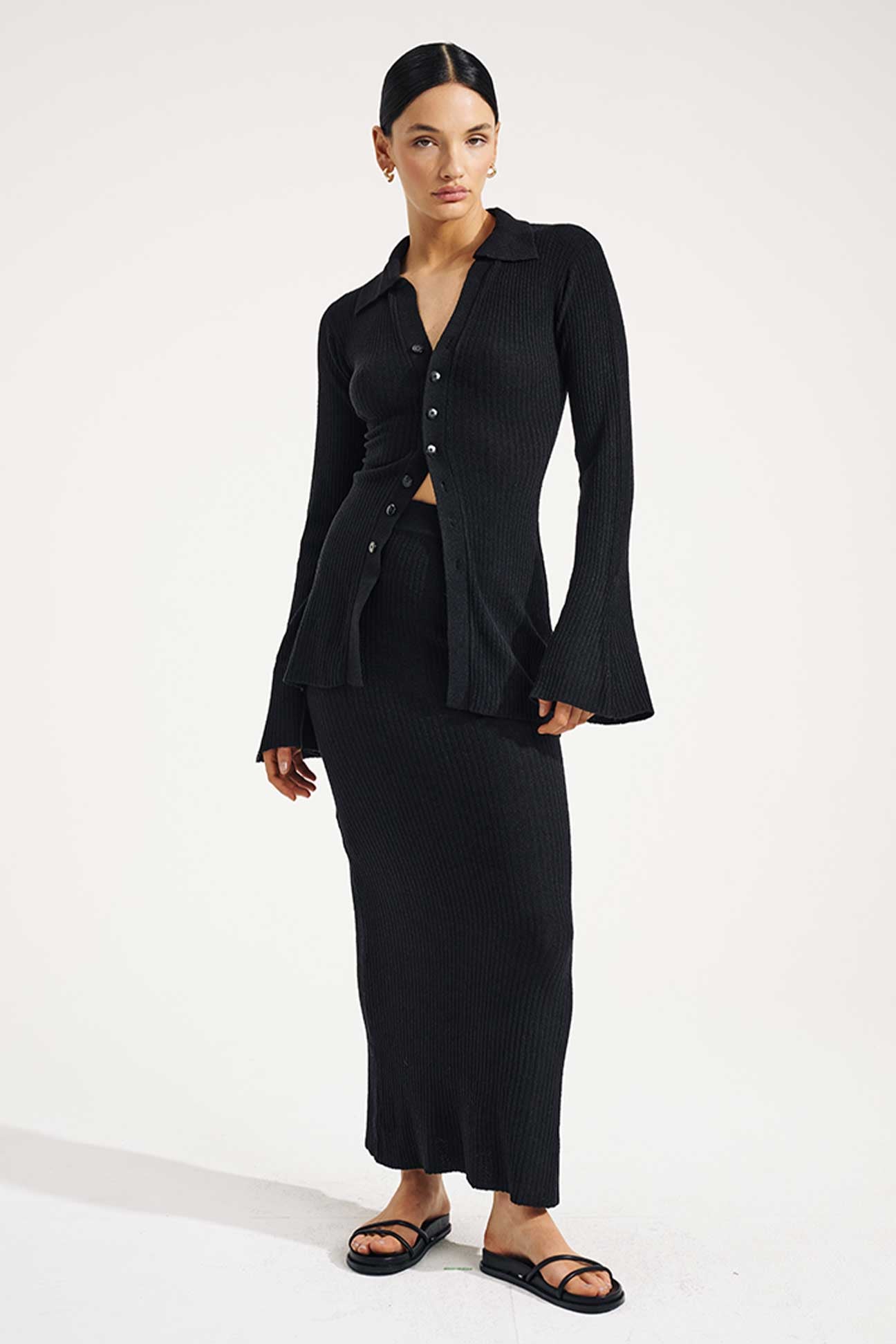 Woman wearing a black outfit with a long skirt and jacket on a white background