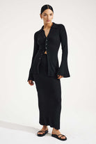 Woman wearing a black outfit with a long skirt and jacket on a white background