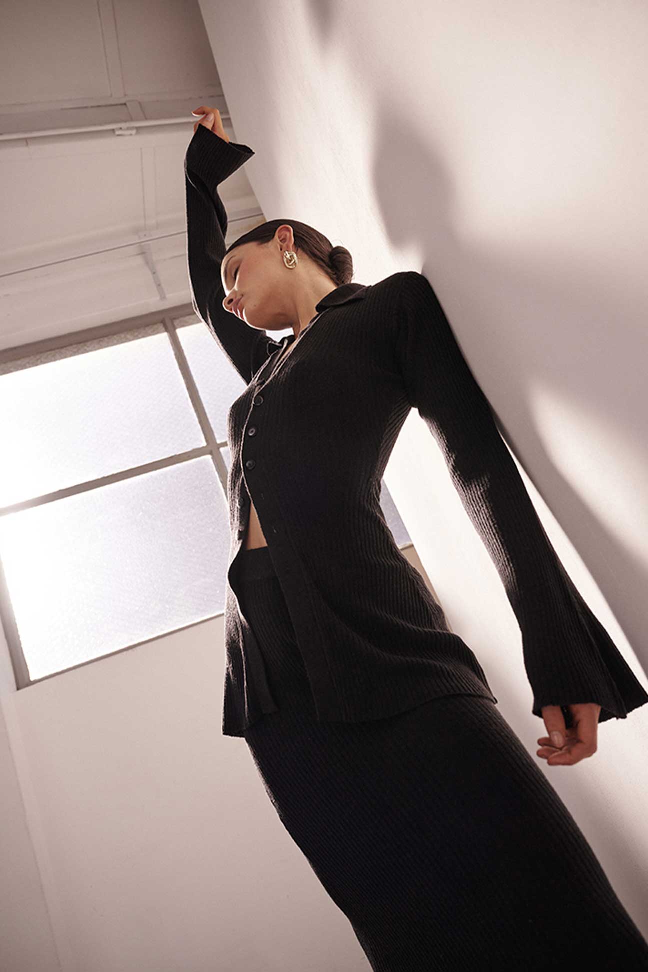 Woman in a black suit standing against a white wall with a window in the background