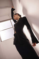 Woman in a black suit standing against a white wall with a window in the background