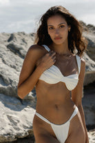 Woman in a white bikini standing on a rocky beach.