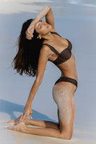Woman in a brown bikini posing on a beach with clear blue sky.