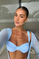 Woman wearing a light blue bikini with a sheer blue cardigan indoors.