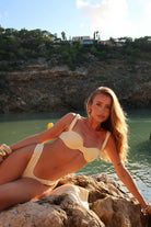 Woman in a bikini lying on rocks by a body of water with cliffs in the background