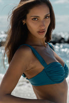 Woman wearing a teal bikini on a beach with water and sky in the background