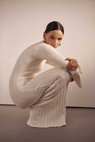 Woman in a white ribbed knit outfit posing against a plain background