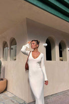 Woman in a white dress standing in front of a building with arched windows.