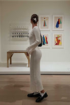 Woman in a white dress standing in an art gallery with colorful abstract paintings on the wall.