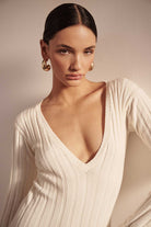 Woman wearing a white ribbed sweater against a neutral background