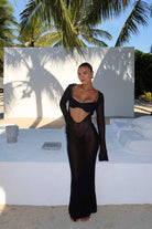 Woman in a black sheer dress standing outdoors with palm trees in the background