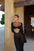 Woman in a black dress standing next to a wooden structure with a thatched roof.