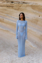 Woman wearing a light blue dress against a textured beige wall.