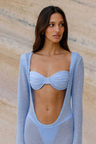Woman wearing a light blue bikini and cover-up against a beige wall.
