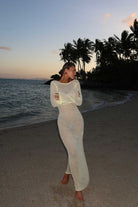 Woman in a yellow dress standing on a beach with palm trees and ocean in the background