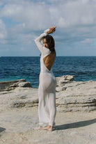 Woman in a white dress standing on a rocky beach with ocean and sky in the background
