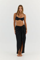 Woman wearing a black bikini and matching black wrap skirt on a white background