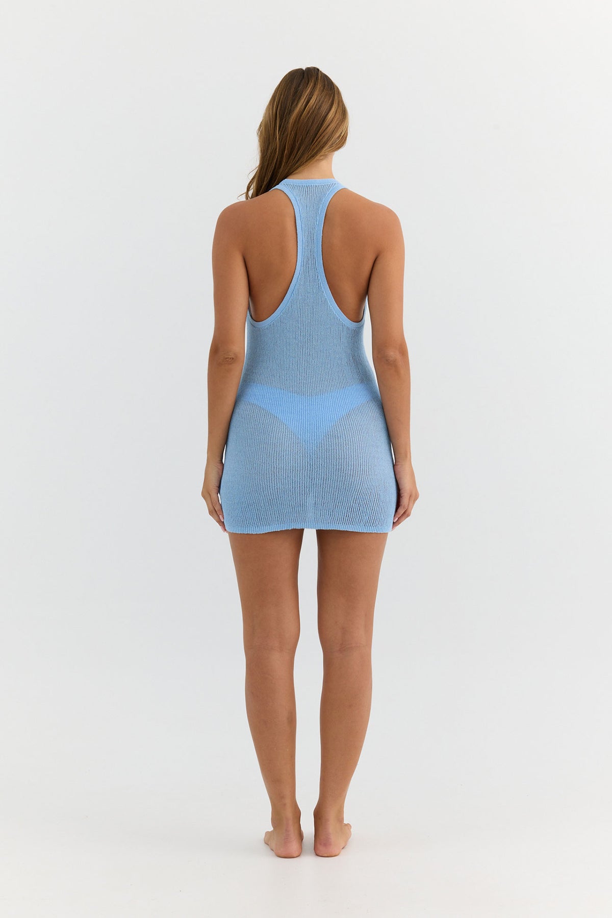 A woman viewed from the back wearing a light blue sleeveless mini dress with a racerback design and a sheer mesh overlay, set against a plain white studio background.