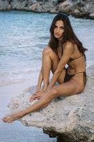 Woman in a black bikini sitting on a rock by the water