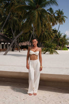 Woman in a white outfit standing on a sandy path with palm trees in the background