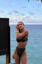 Woman in a brown bikini standing by the ocean with a scenic background