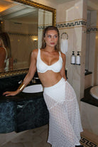 Woman in a white bikini and skirt standing in a bathroom.