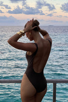 Woman in a black swimsuit standing by the ocean with a sunset in the background