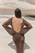 Person wearing a brown swimsuit with a sheer overlay on a sandy background