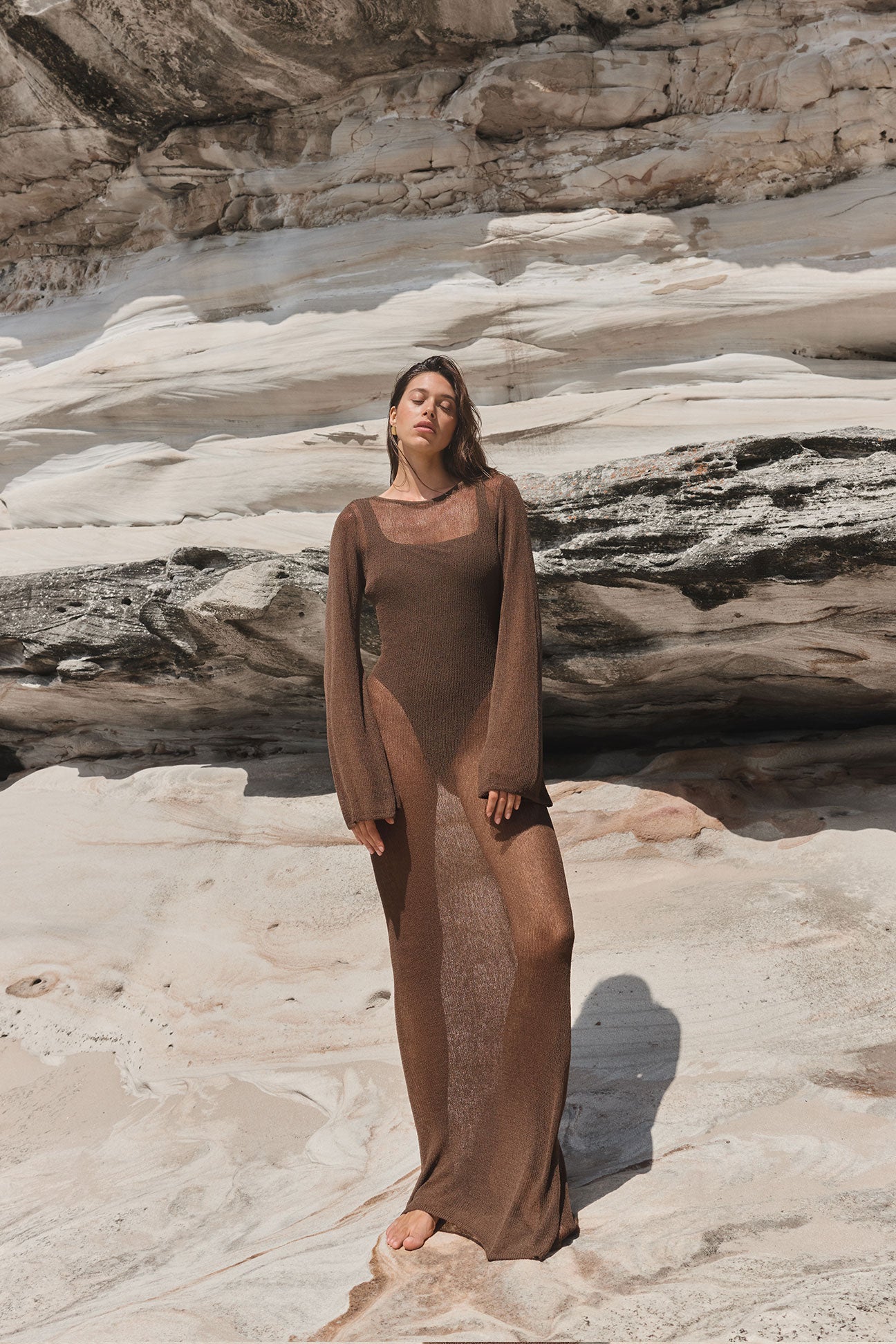 Woman in a brown dress standing on a rocky beach