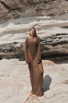 Woman in a brown dress standing on a rocky beach