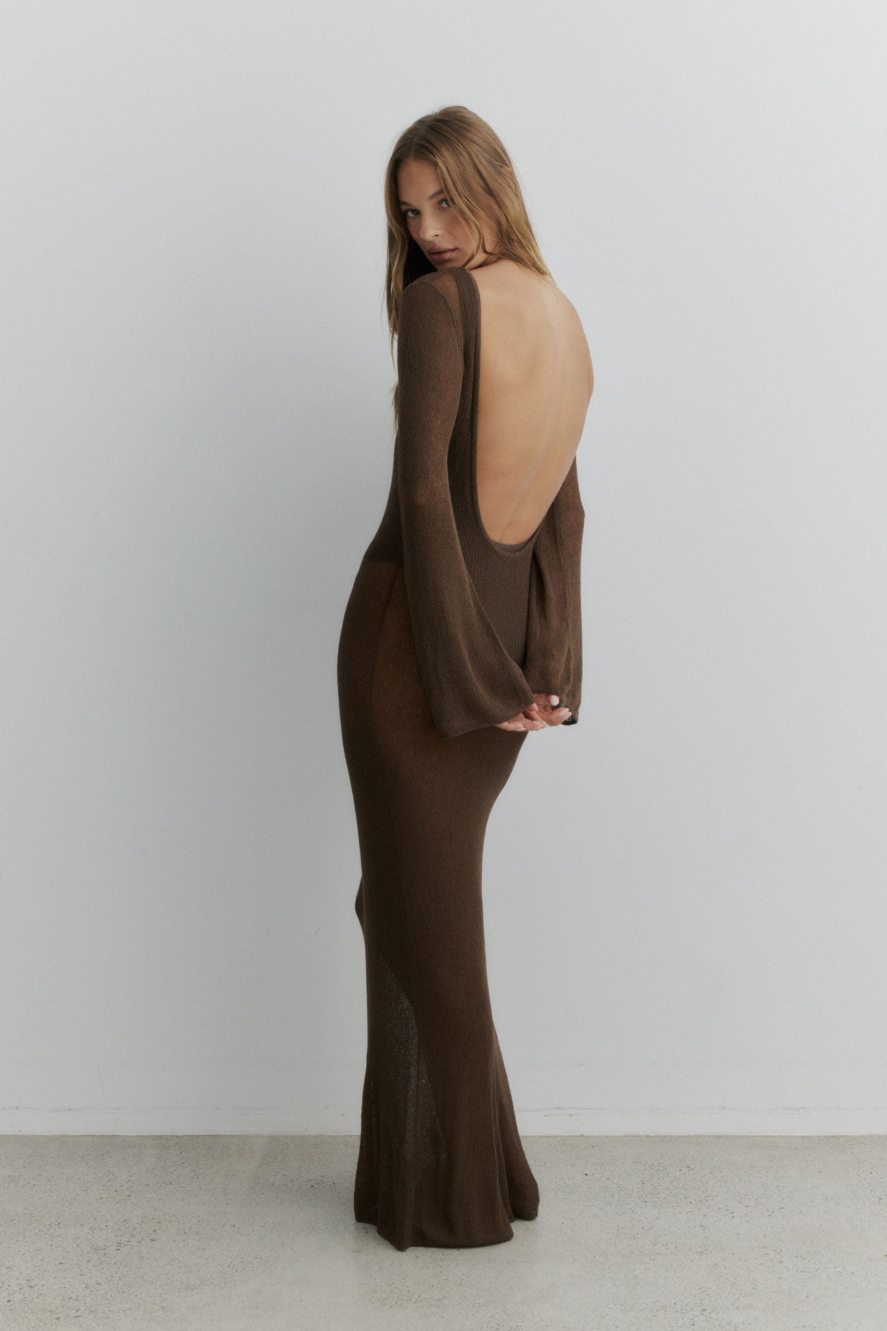 Woman wearing a brown open-back dress against a white background