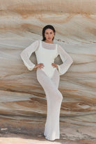 Woman in a white outfit standing against a textured stone wall