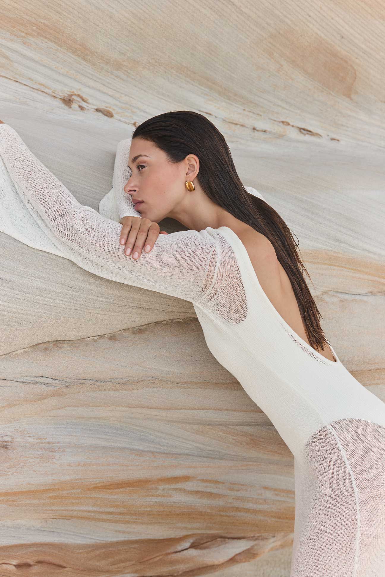 Woman in a white sheer dress lying on a textured beige surface