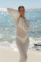 Woman wrapped in a white blanket on a beach with ocean in the background