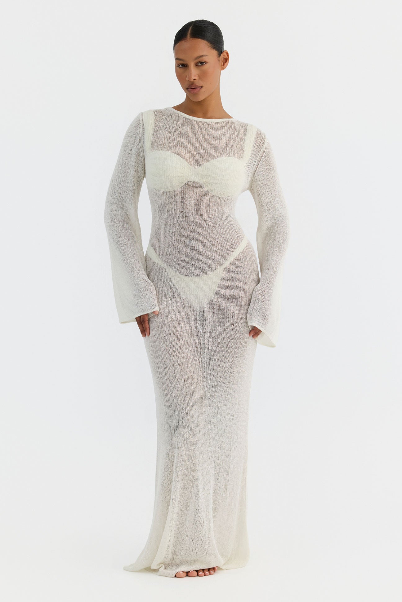 Woman wearing a long, light gray knit dress with a white abstract design on a white background