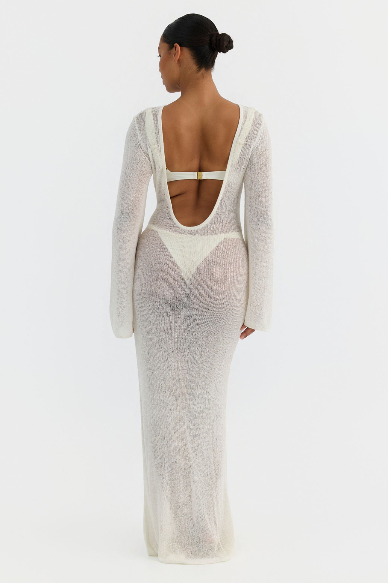 Woman wearing a sheer white dress with long sleeves on a white background