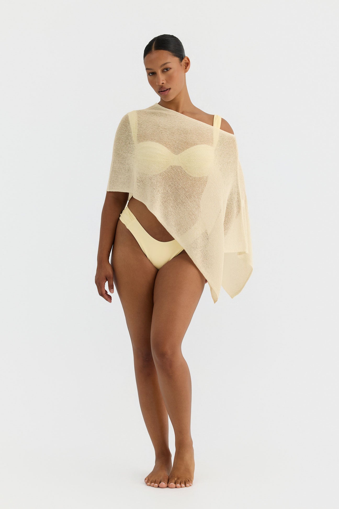 Woman wearing a butter yellow knit poncho on a white background