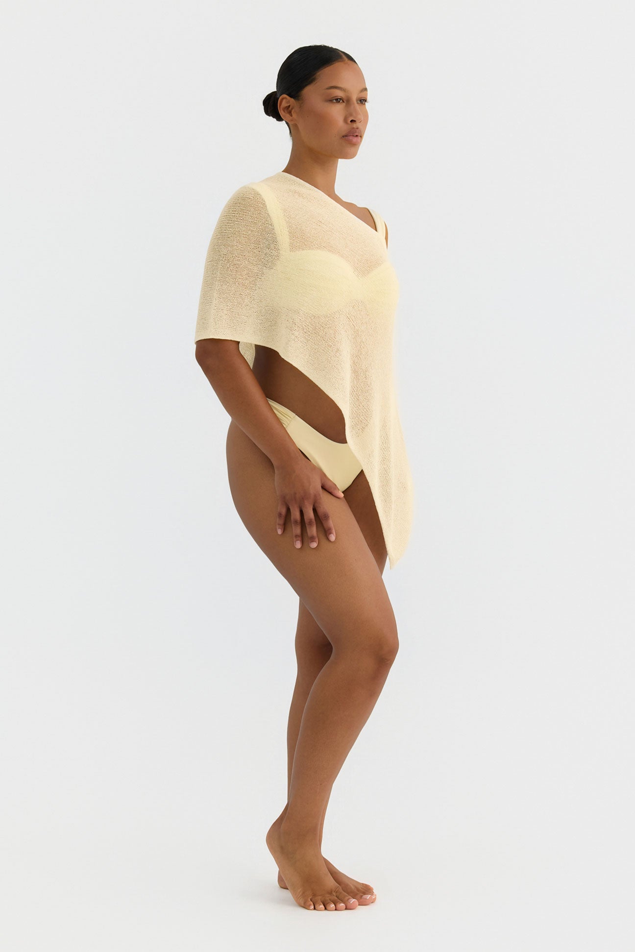Woman wearing a butter yellow knit poncho on a white background