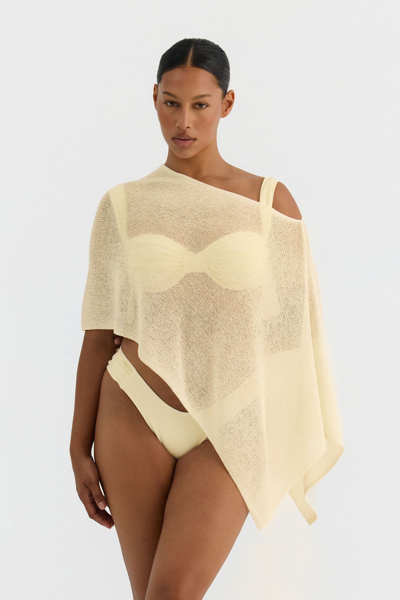Woman wearing a butter yellow knit poncho on a white background