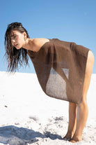 Woman wearing a brown dress on a white sandy beach with blue sky.