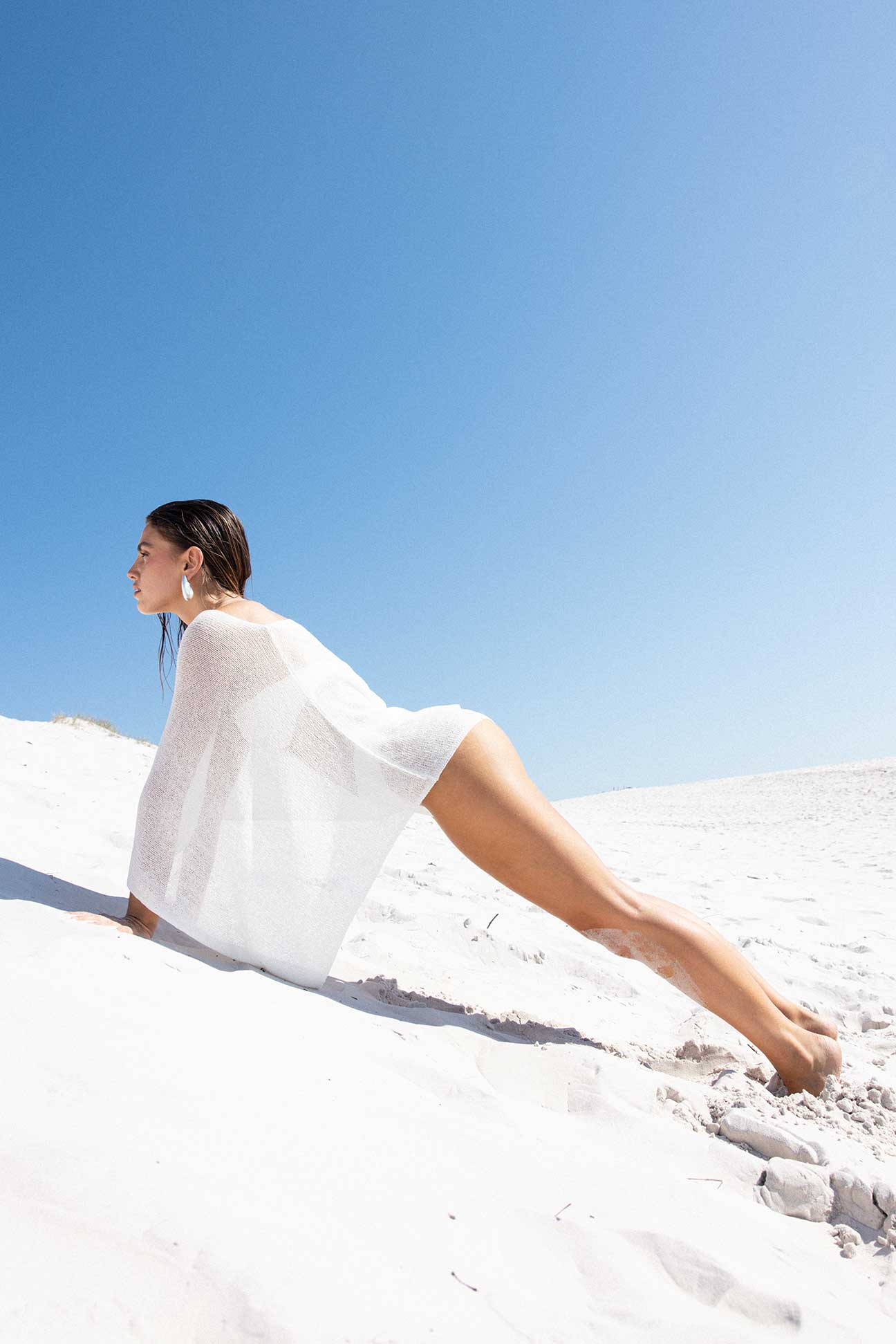 Woman in a white dress sitting on a white sand dune with a clear blue sky.