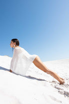 Woman in a white dress sitting on a white sand dune with a clear blue sky.