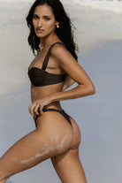 Woman in a brown bikini standing on a beach with sand on her legs.