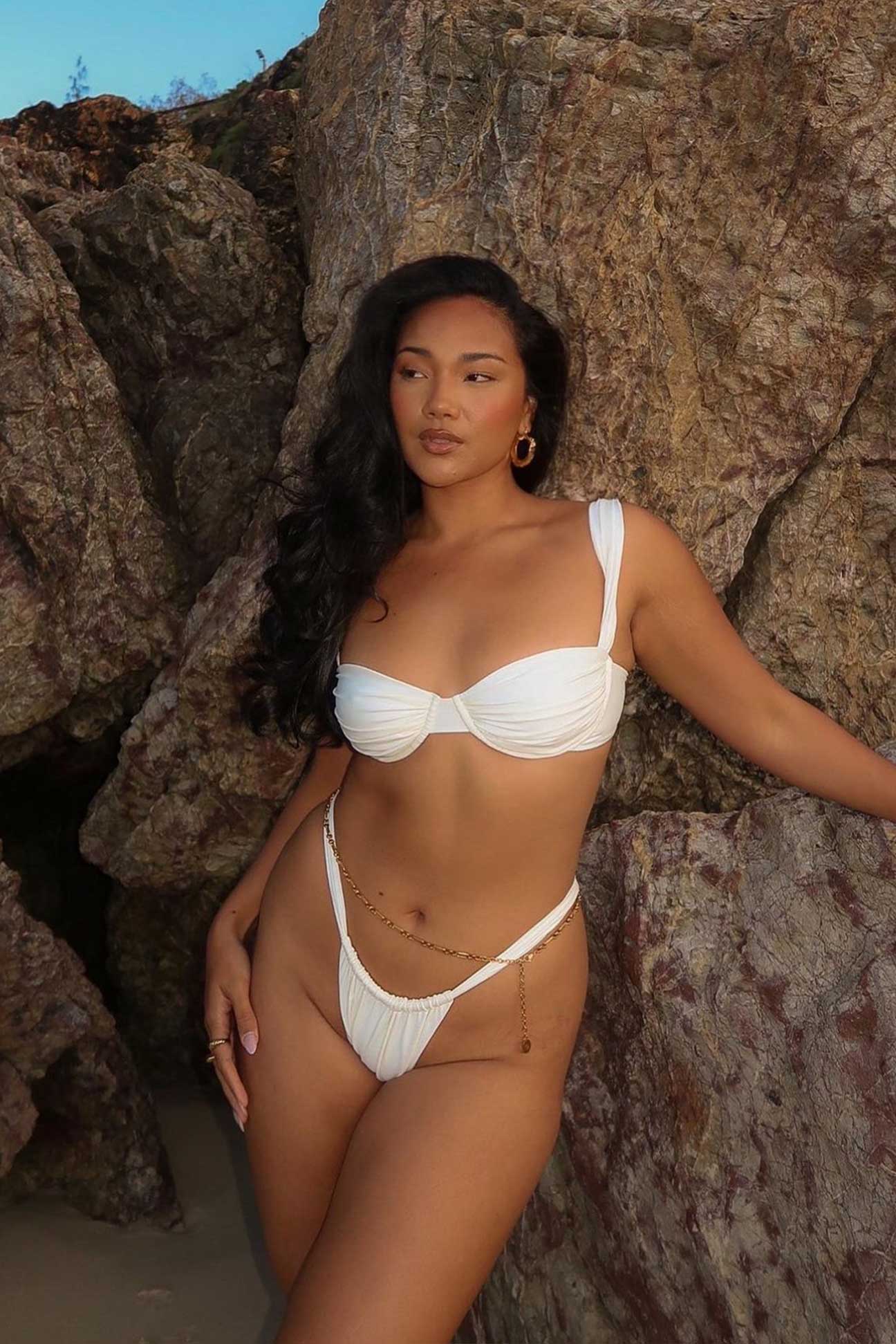 Woman in a ivory bikini standing against rocky terrain