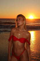 Woman in a red bikini standing on a beach at sunset.