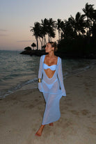 Woman in a white cover-up standing on a beach with palm trees in the background