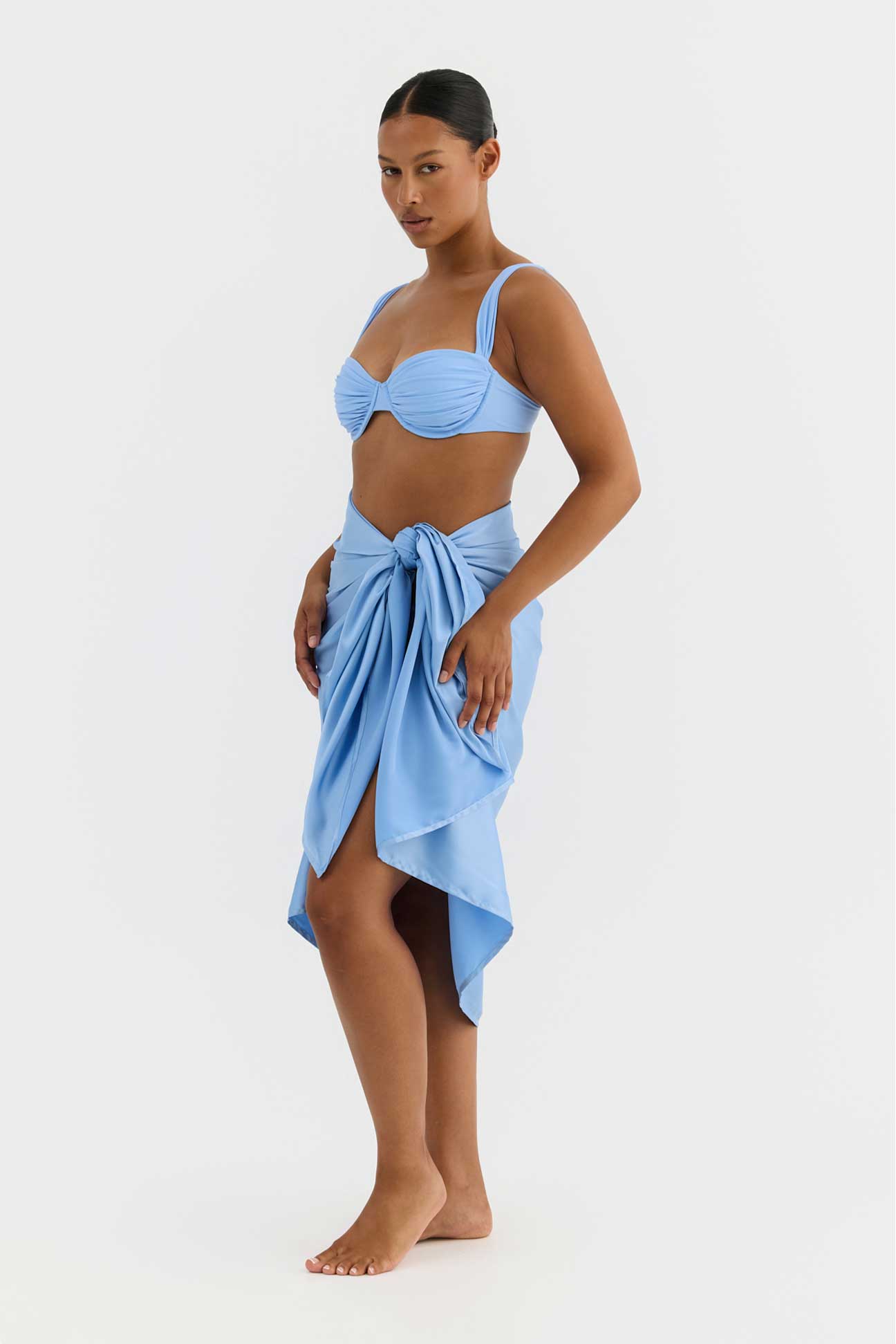 Woman wearing a blue bikini and matching sarong on a white background